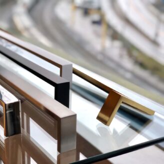 5 handles on a glass table shown in the following finishes: matte black, satin white, satin brass, polished stainless and brushed stainless.