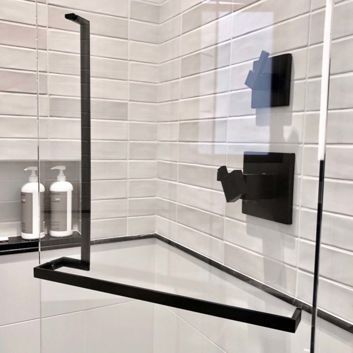 A back to back black shower door handle and towel bar mounted on a glass shower door.