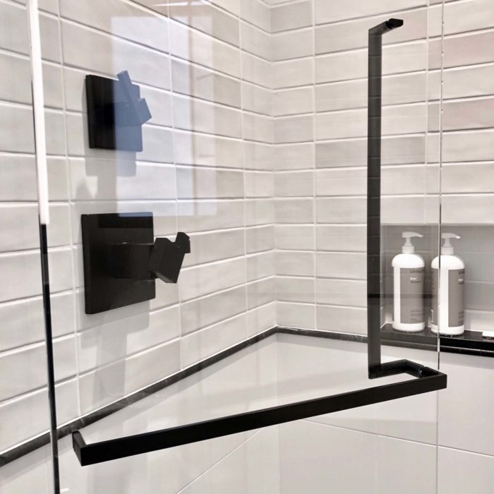A back to back black shower door handle and towel bar mounted on a glass shower door.