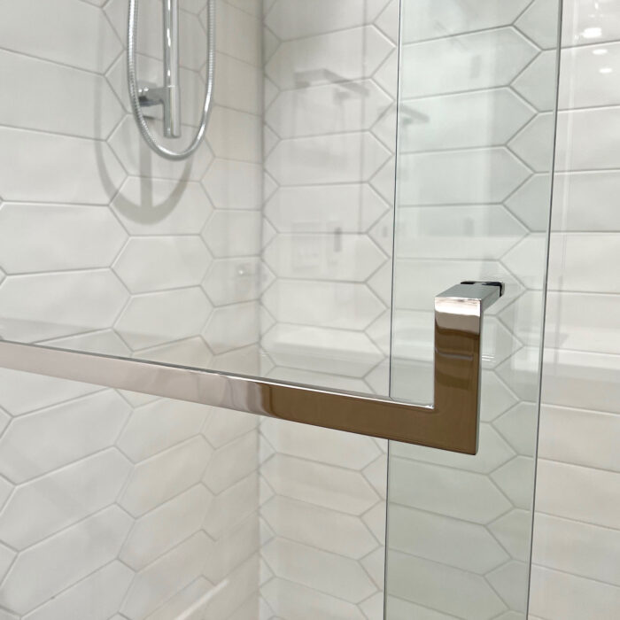 A polished stainless glass door towel bar mounted in a contemporary shower with white hexagon tiles.