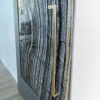 A satin brass barn door handle installed on a sliding stone barn door.