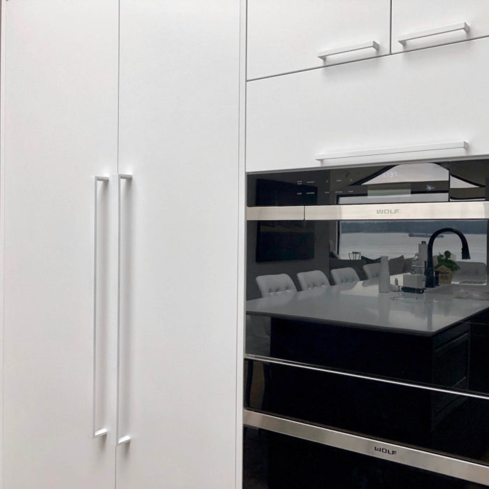 White appliance door handles mounted on a Miele panel ready refrigerator and freezer next to double Wolf wall ovens.