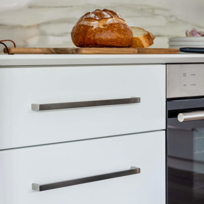 Brushed stainless steel cabinet pulls mounted on white contemporary drawers with a fresh loaf of artisan bread above.
