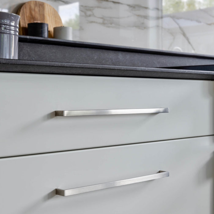 Brushed stainless steel cabinet pulls mounted on white contemporary drawers.