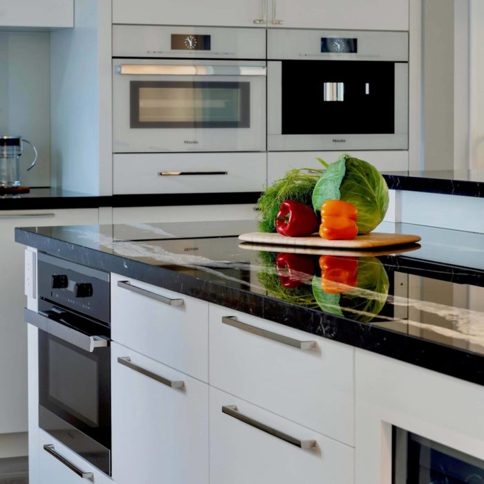 A contemporary kitchen design using Miele appliances, black countertops and polished stainless cabinet pulls.