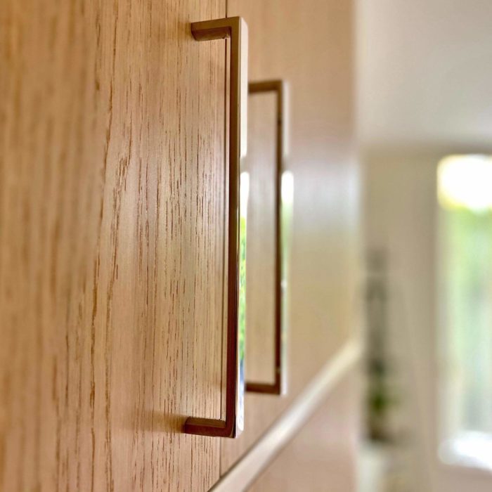 A close up view of two modern cabinet pulls mounted on oak doors.