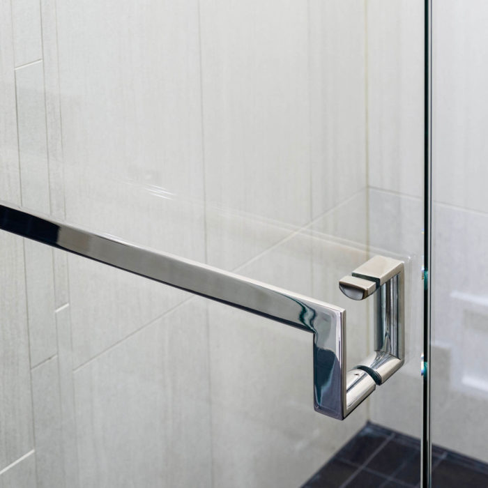 A polished stainless steel shower door handle and towel bar mounted on a shower door.