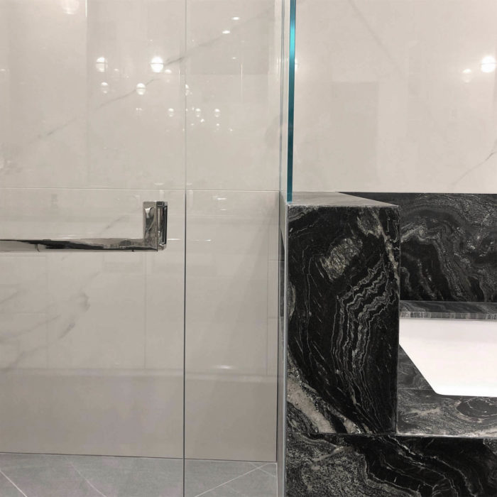 A polished stainless shower door handle and towel bar mounted next to a black marble bathtub.