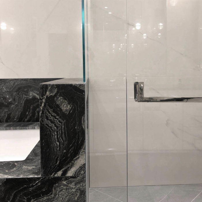 A polished stainless shower door handle and towel bar mounted next to a black marble bathtub.