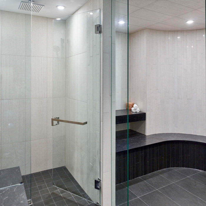 A steam room glass door mounted with polished stainless handles and towel bar.