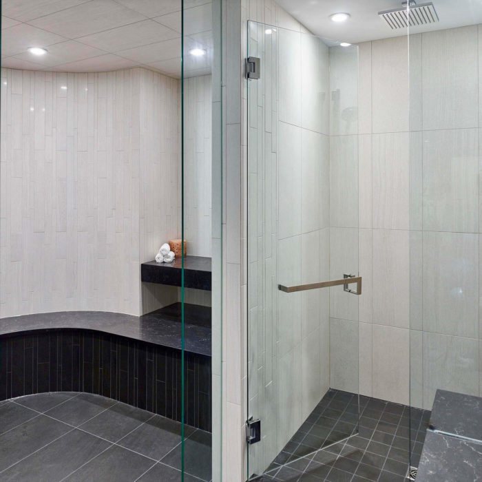 A steam room glass door mounted with polished stainless handles and towel bar.