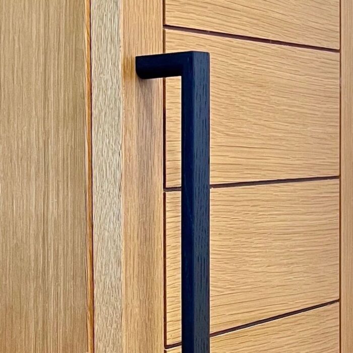 Contemporary black wooden handle by JWL Hardware on a light oak cabinet door, showcasing minimalist design and functionality.