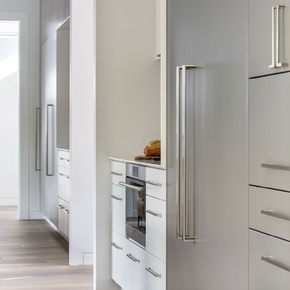 Sleek stainless steel kitchen handles on white cabinets by JWL Hardware, enhancing a modern and minimalist kitchen design.