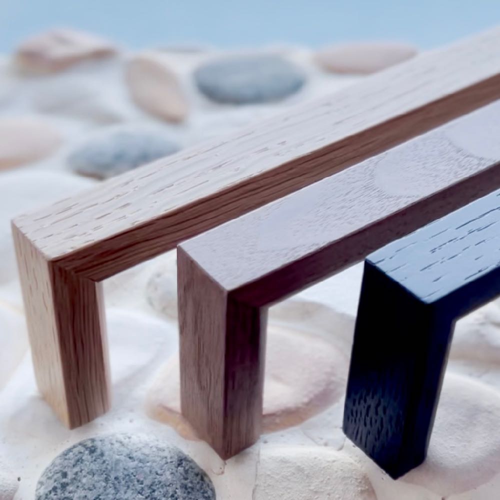 Assortment of JWL Hardware's premium wooden handles in various finishes displayed on a sandy beach background, highlighting the natural texture and color options.