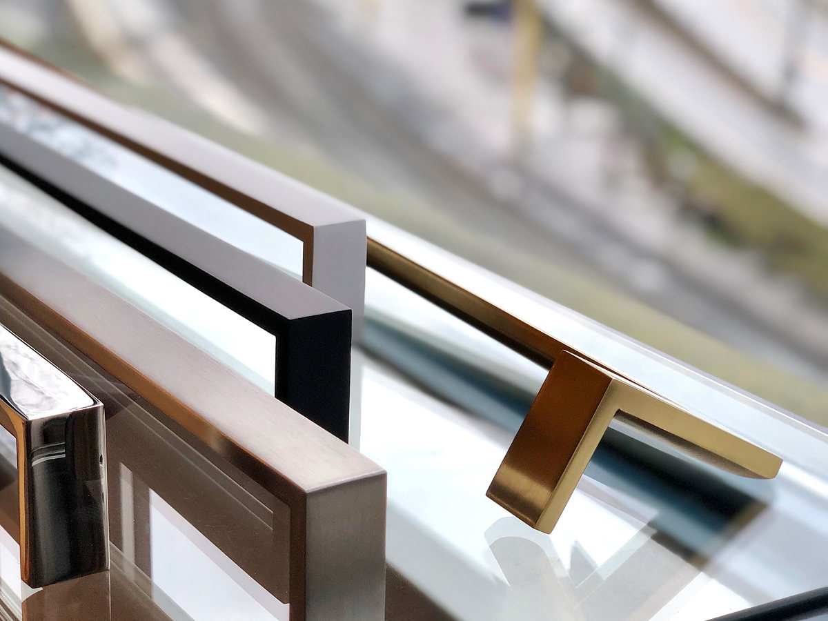 Glass door handles in satin brass, matte black, white and brushed stainless steel on a glass door.