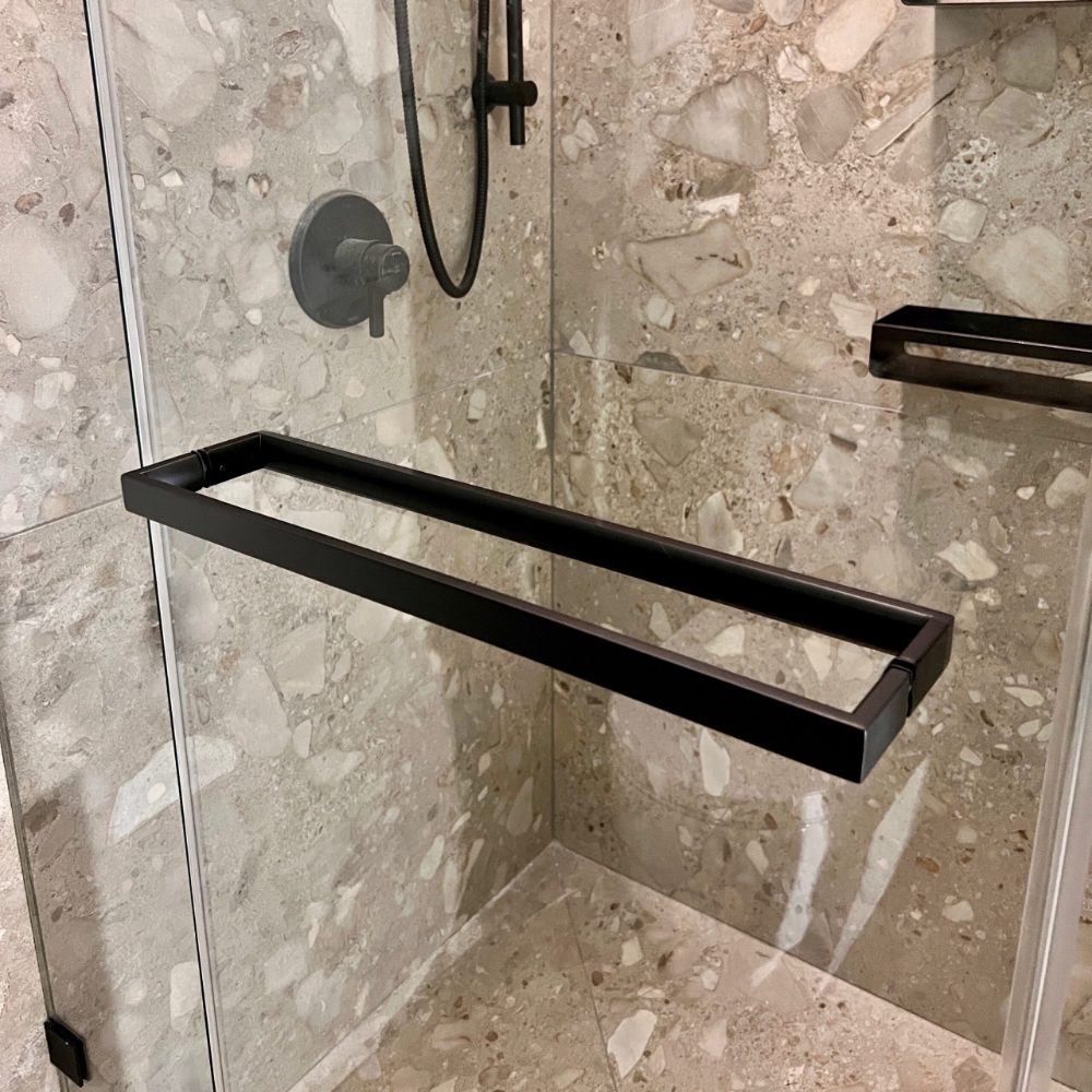 A matte black shower door handle installed on a modern shower door enclosure. The shower door handle can also be used as a towel bar. The size is 18 from centre to centre