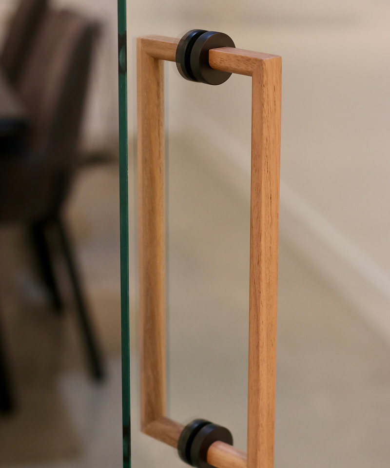 Solid oak back-to-back glass door handle with matte black fittings on a glass door.