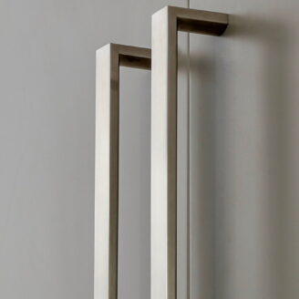 Two tall brushed stainless steel door handles mounted on grey cabinet doors.
