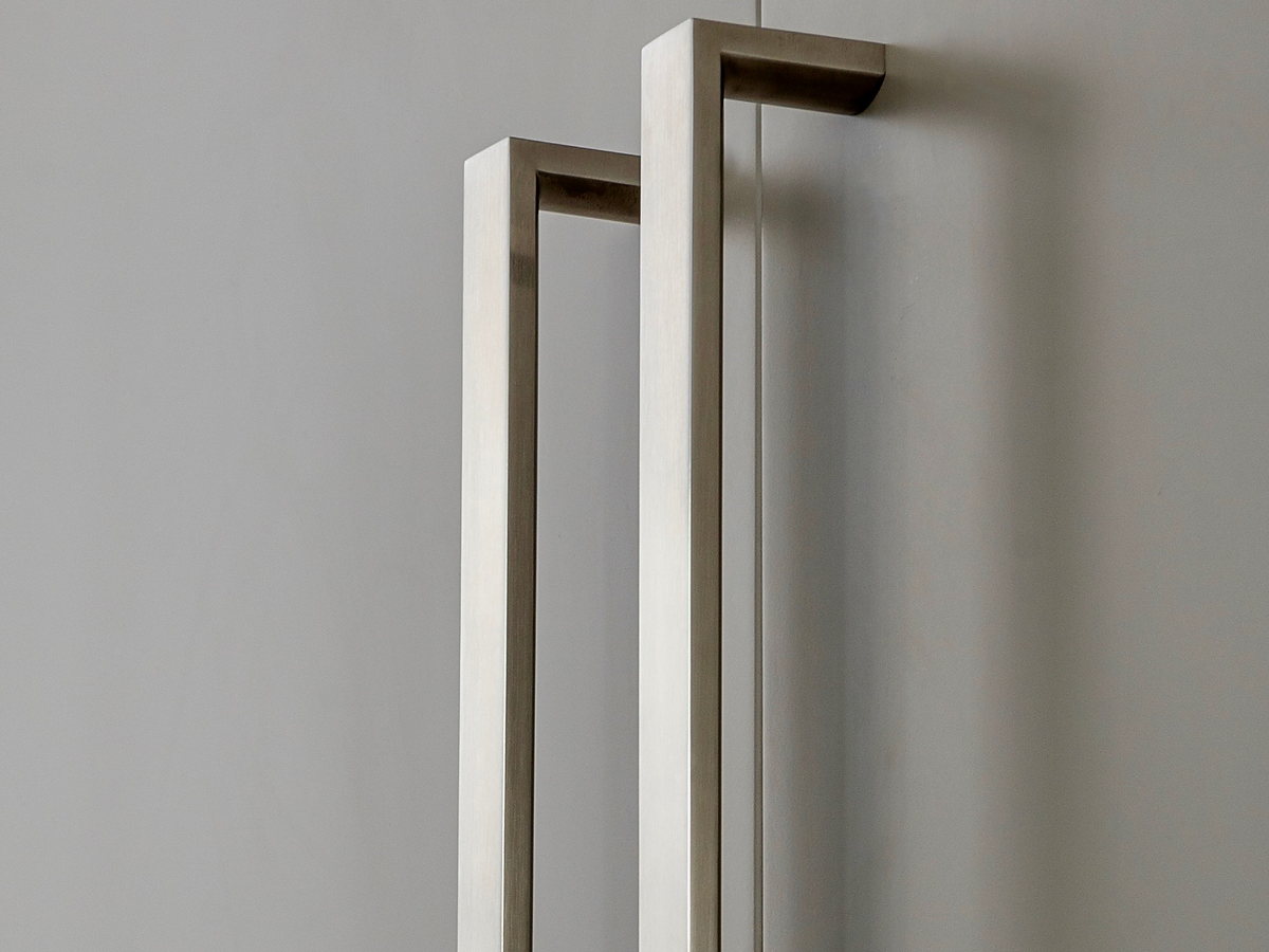 Two tall brushed stainless steel door handles mounted on grey cabinet doors.