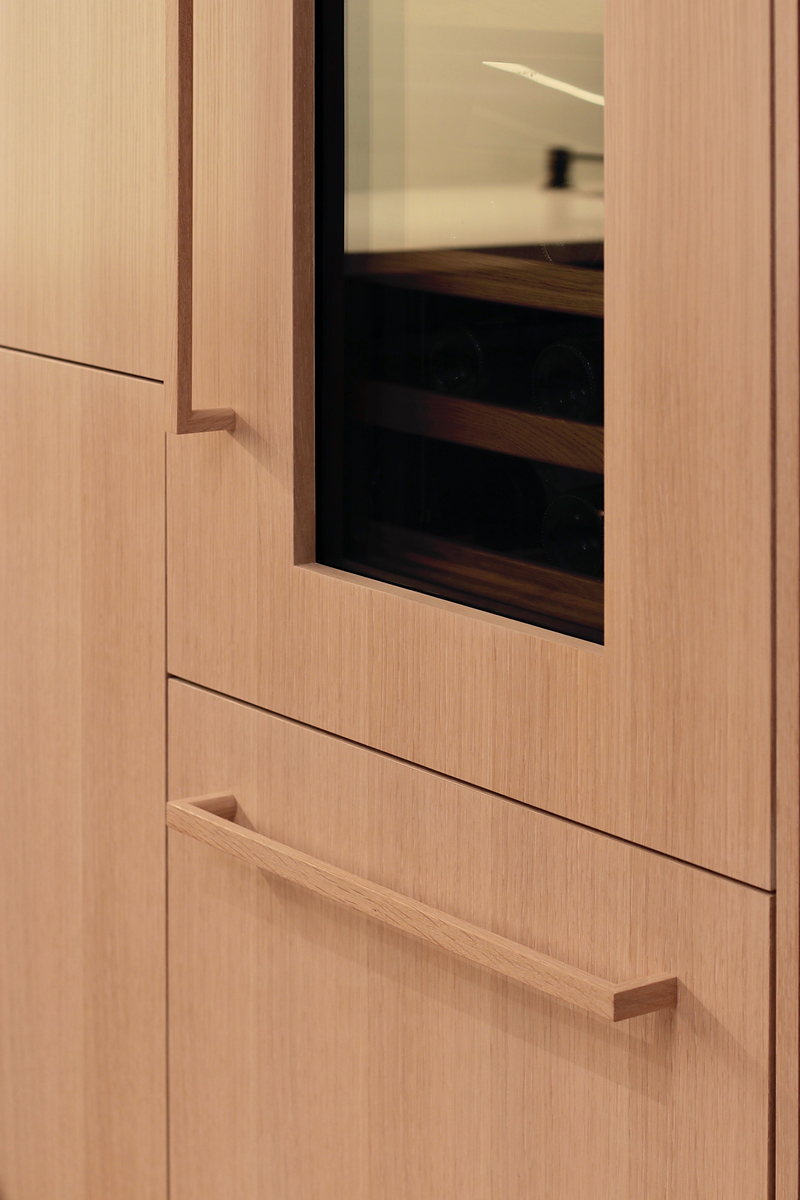 White oak appliance handle on a panel-ready wine fridge in an oak kitchen.